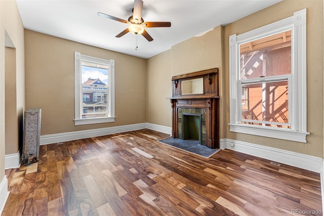 unfurnished living room with a ceiling fan, a tile fireplace, baseboards, and wood finished floors