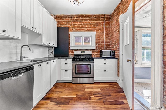 kitchen with brick wall, appliances with stainless steel finishes, dark countertops, and a sink