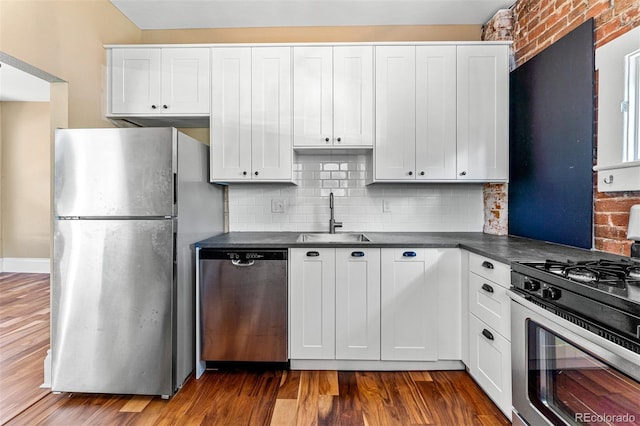 kitchen featuring stainless steel appliances, dark wood-type flooring, a sink, white cabinets, and dark countertops