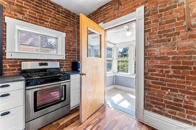 kitchen with stainless steel gas stove, white cabinets, dark countertops, brick wall, and wood finished floors