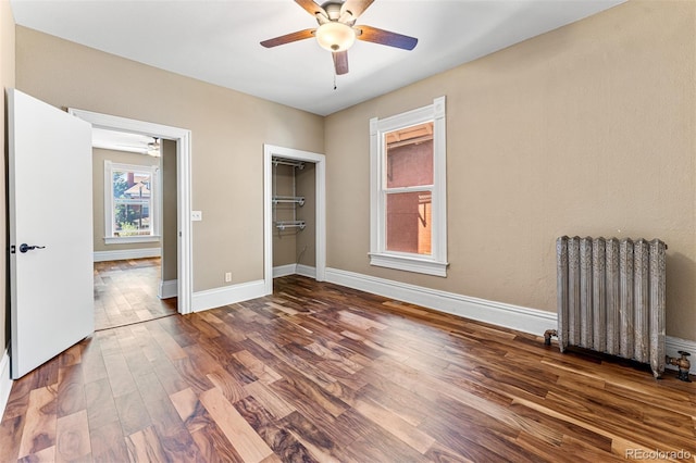 unfurnished bedroom featuring baseboards, radiator, ceiling fan, wood finished floors, and a closet