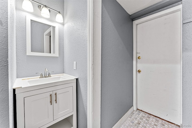 bathroom with a textured wall, baseboards, and vanity