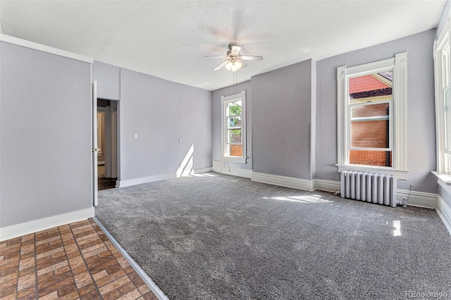 empty room featuring a ceiling fan, radiator, a textured ceiling, and baseboards