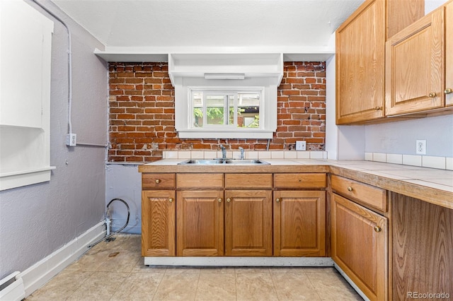 kitchen featuring light tile patterned floors, a baseboard heating unit, a sink, brick wall, and baseboards