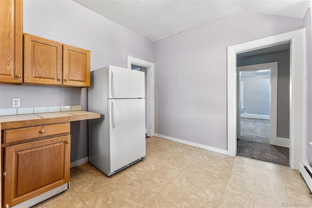 kitchen with lofted ceiling, freestanding refrigerator, brown cabinetry, and tile countertops