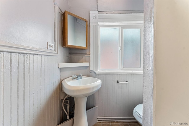 half bathroom featuring wooden walls, wainscoting, toilet, and tile patterned floors