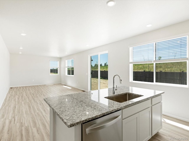 7324 27th Street Ln, Greeley, CO 80634 - kitchen with stainless steel dishwasher, a sink, an island with sink, light stone counters, and light wood-style floors