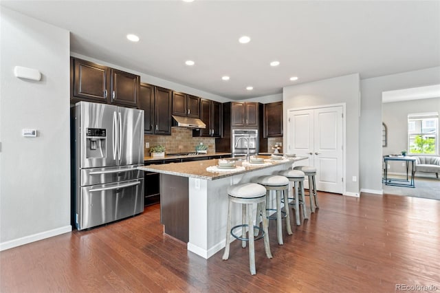 18180 W 84th Pl, Arvada, CO 80007 - kitchen featuring appliances with stainless steel finishes, under cabinet range hood, a breakfast bar area, tasteful backsplash, and dark wood finished floors