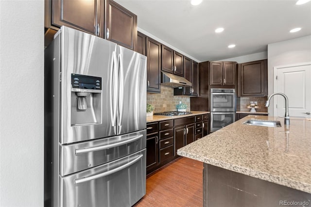 18180 W 84th Pl, Arvada, CO 80007 - kitchen with stainless steel appliances, under cabinet range hood, decorative backsplash, dark brown cabinets, and recessed lighting