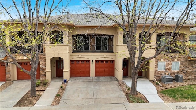 mediterranean / spanish-style house featuring a balcony, driveway, an attached garage, central AC, and stucco siding