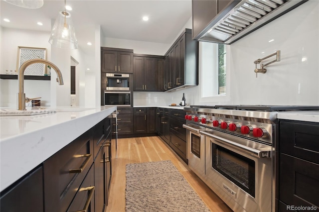 kitchen with light stone countertops, dark brown cabinetry, ventilation hood, range with two ovens, and light hardwood / wood-style floors