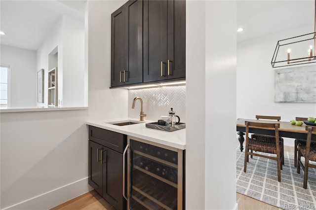 bar featuring decorative backsplash, dark brown cabinets, beverage cooler, sink, and light hardwood / wood-style flooring