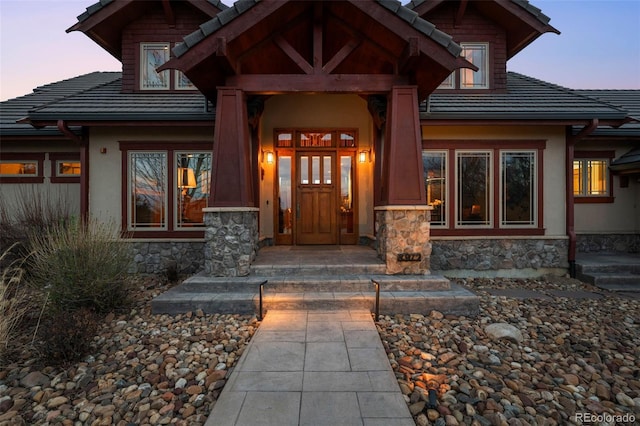 doorway to property featuring stucco siding, a tiled roof, and stone siding