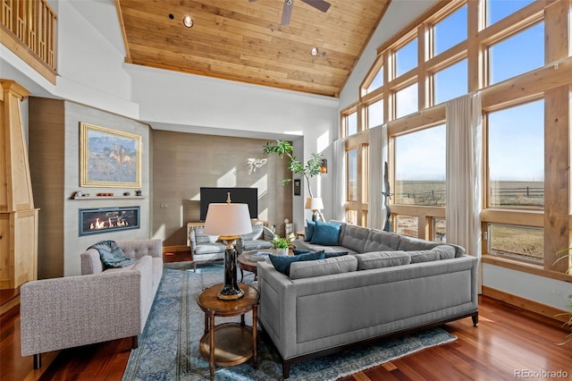 living room with ceiling fan, high vaulted ceiling, a glass covered fireplace, wood finished floors, and wood ceiling