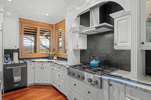 kitchen with a sink, wall chimney exhaust hood, stainless steel appliances, white cabinetry, and decorative backsplash