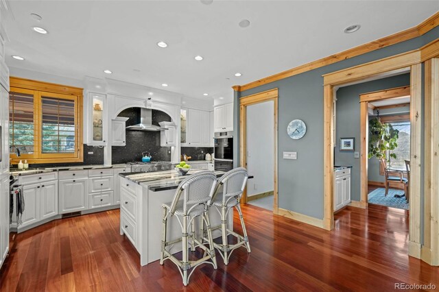 kitchen with decorative backsplash, baseboards, wall chimney range hood, recessed lighting, and white cabinets