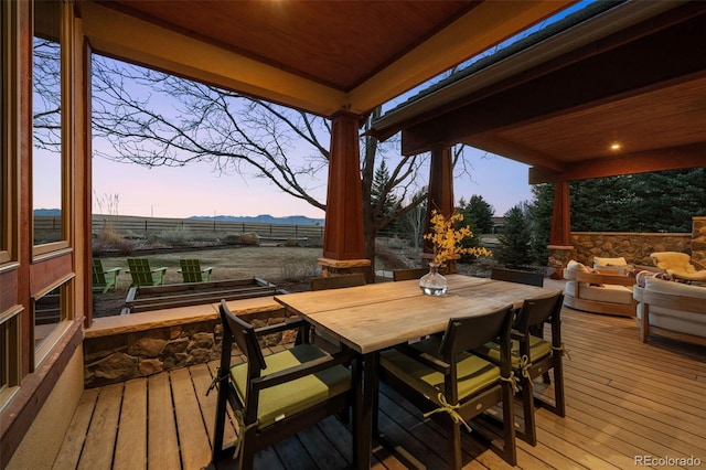 deck at dusk with fence, a mountain view, and outdoor dining area