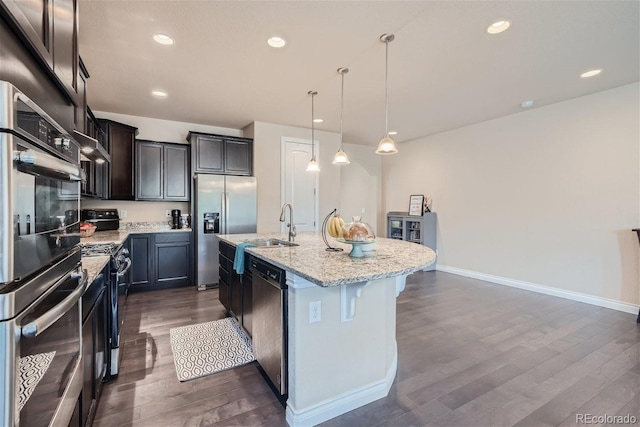 kitchen with decorative light fixtures, dark hardwood / wood-style floors, a breakfast bar, appliances with stainless steel finishes, and a kitchen island with sink