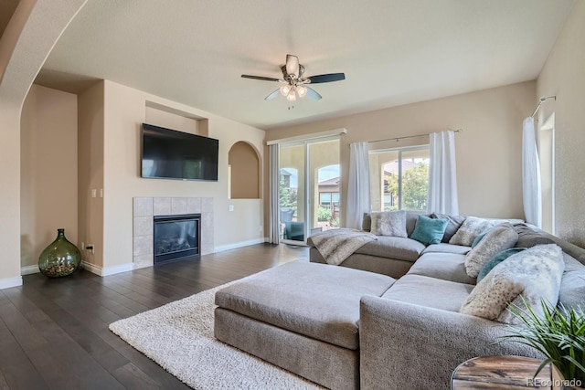 living room with dark wood-type flooring, a tiled fireplace, and ceiling fan