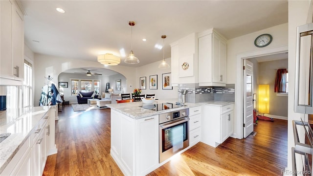 kitchen with arched walkways, light wood finished floors, backsplash, oven, and black electric cooktop