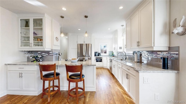 kitchen featuring stainless steel appliances, glass insert cabinets, a sink, light stone countertops, and a peninsula