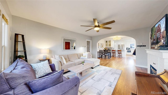 living area featuring arched walkways, ceiling fan, baseboards, and wood finished floors