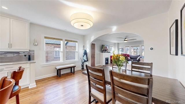 dining area with light wood-style floors, arched walkways, a glass covered fireplace, and baseboards