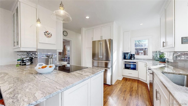 kitchen featuring stainless steel appliances, a peninsula, wood finished floors, white cabinets, and backsplash