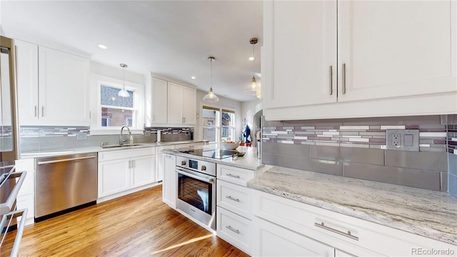 kitchen featuring light wood finished floors, a sink, stainless steel appliances, white cabinetry, and backsplash