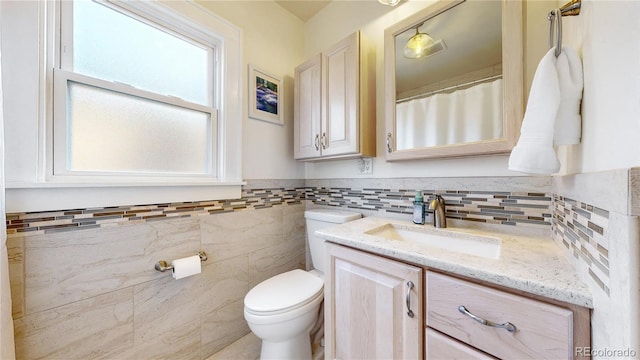 full bathroom with toilet, a wainscoted wall, tile walls, and vanity