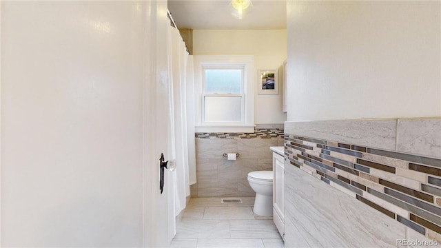 bathroom with a wainscoted wall, toilet, and tile walls