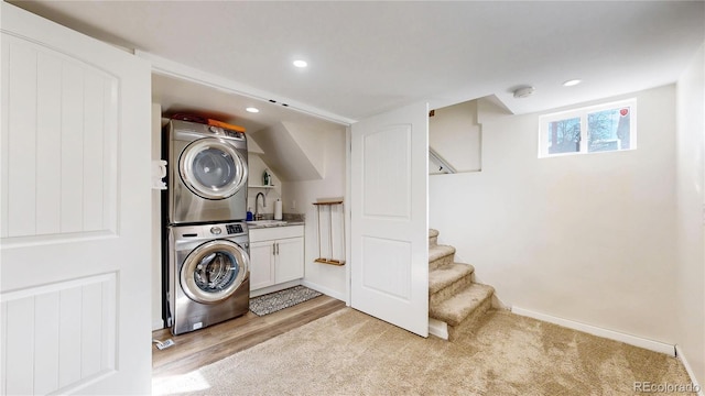 clothes washing area featuring stacked washer and dryer, baseboards, light wood-style flooring, a sink, and recessed lighting