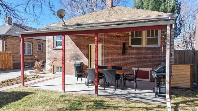 rear view of property with a patio, brick siding, roof with shingles, and fence