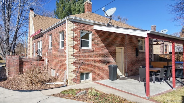 rear view of house featuring a patio, brick siding, fence, roof with shingles, and a chimney