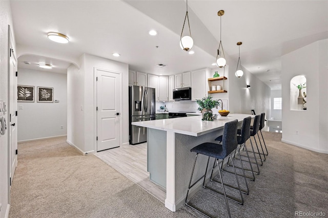 kitchen with appliances with stainless steel finishes, light colored carpet, a kitchen breakfast bar, open shelves, and light countertops