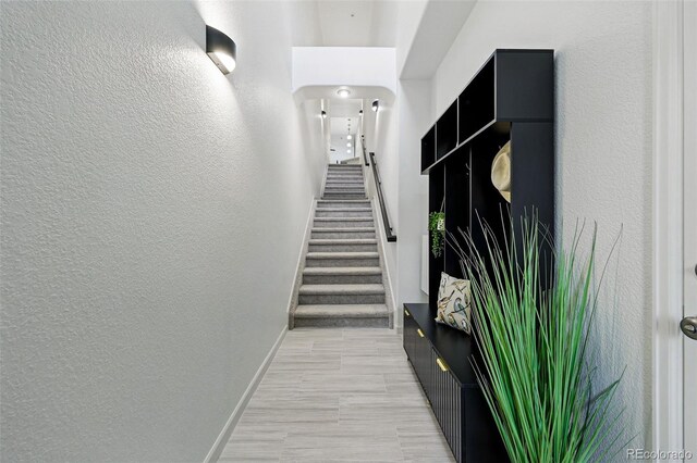hallway with a textured wall, baseboards, and stairway