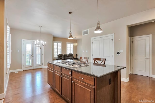 kitchen with stainless steel gas stovetop, light wood finished floors, a center island, stone countertops, and hanging light fixtures