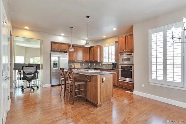 kitchen with stainless steel appliances, a center island, brown cabinetry, a kitchen bar, and baseboards