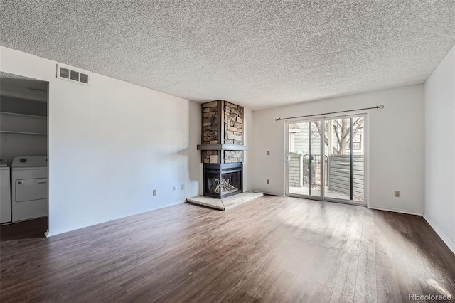 unfurnished living room with hardwood / wood-style floors, washing machine and dryer, a textured ceiling, and a stone fireplace