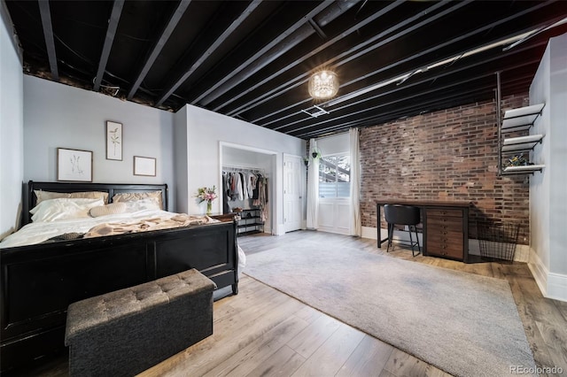 bedroom featuring a spacious closet, light hardwood / wood-style floors, a closet, and brick wall