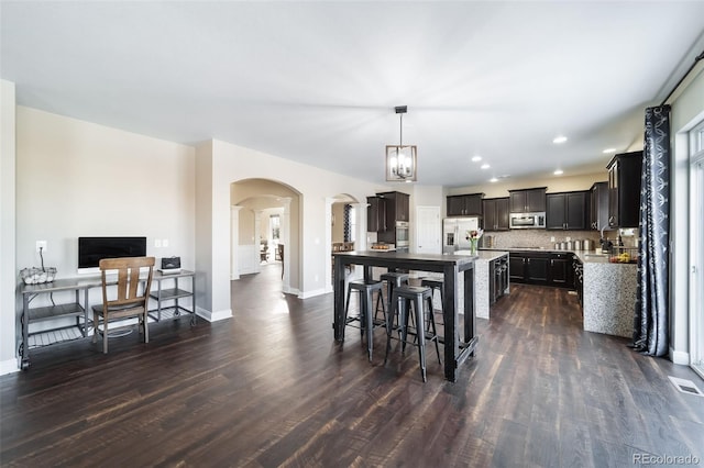 kitchen featuring dark wood-type flooring, stainless steel appliances, decorative light fixtures, and backsplash