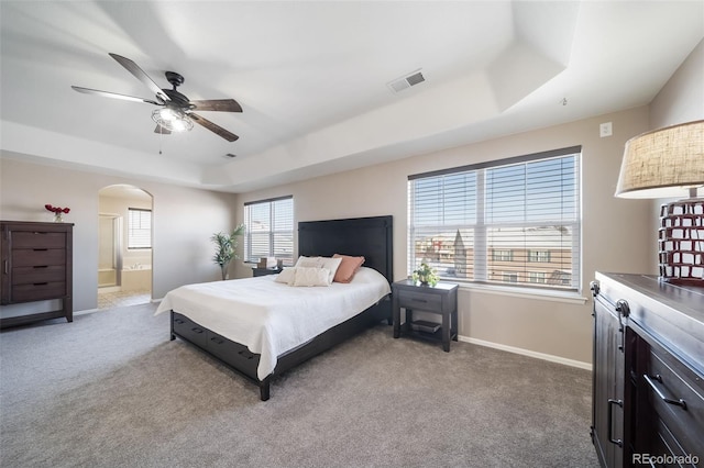 bedroom with a tray ceiling, ensuite bathroom, ceiling fan, and carpet