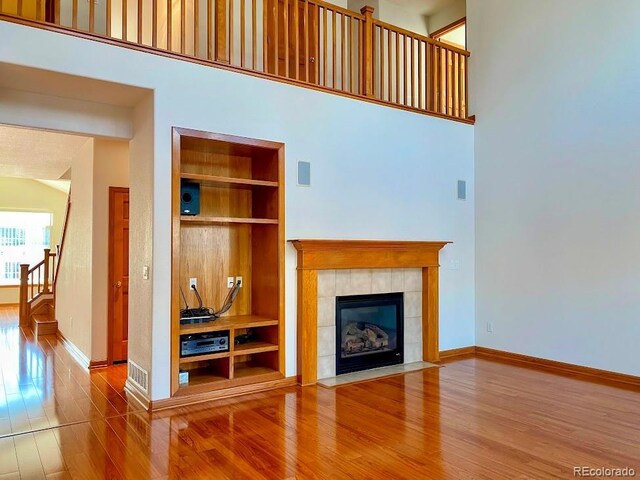 1022 Morning Dove Dr, Longmont, CO 80504 - living room featuring built in shelves, wood finished floors, a tile fireplace, baseboards, and a high ceiling
