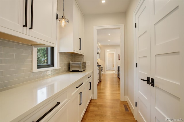 bar featuring pendant lighting, decorative backsplash, light hardwood / wood-style flooring, and white cabinets