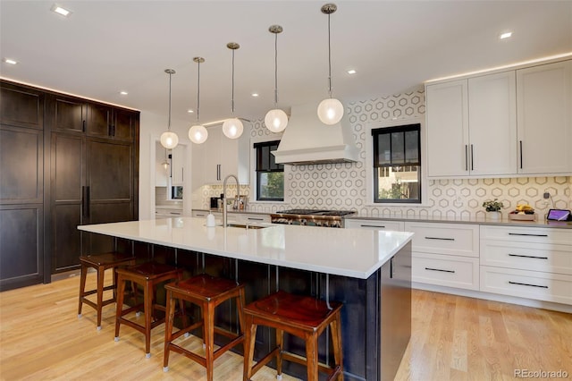 kitchen with premium range hood, sink, pendant lighting, and an island with sink