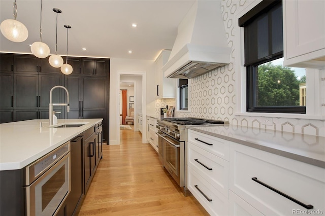 kitchen with pendant lighting, sink, white cabinets, stainless steel appliances, and custom range hood