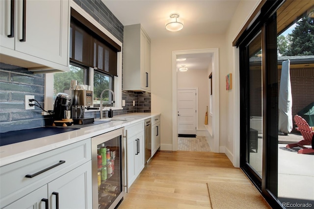 bar featuring sink, light hardwood / wood-style flooring, tasteful backsplash, white cabinets, and beverage cooler