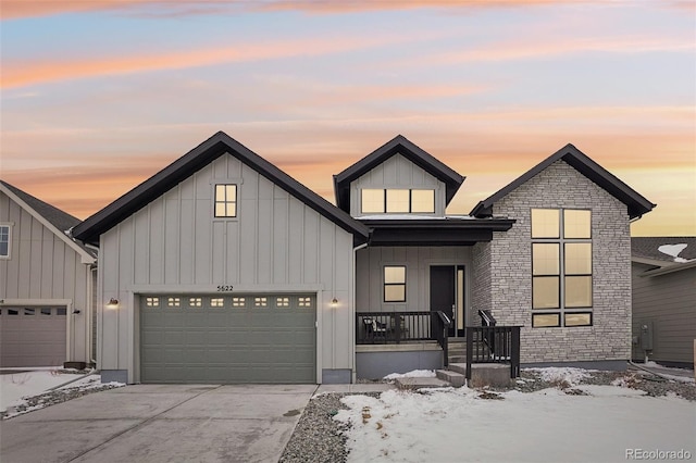 modern inspired farmhouse with covered porch, board and batten siding, a garage, stone siding, and driveway