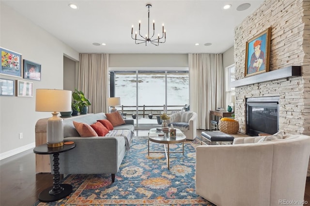 living area with baseboards, wood finished floors, an inviting chandelier, a stone fireplace, and recessed lighting