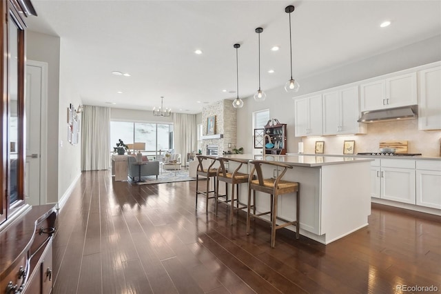 kitchen with a kitchen island, dark wood-style flooring, under cabinet range hood, stainless steel gas cooktop, and backsplash